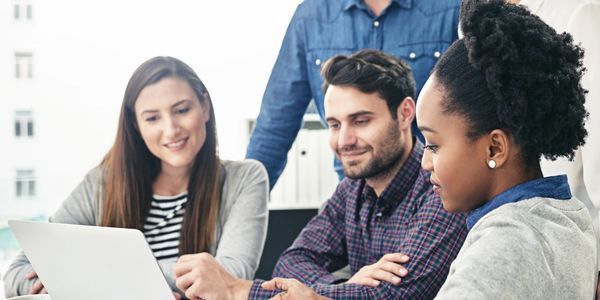 A diverse group of colleagues collaborating over a laptop in a bright office.