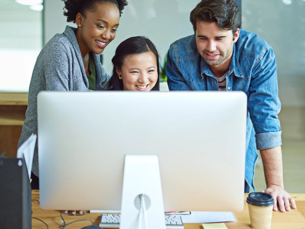 Three colleagues happily collaborating around a computer in an office.