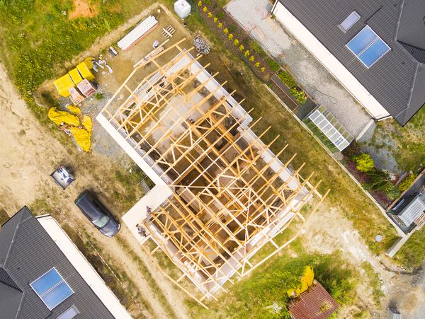 Aerial view of a house under construction with wooden framework and nearby finished houses.