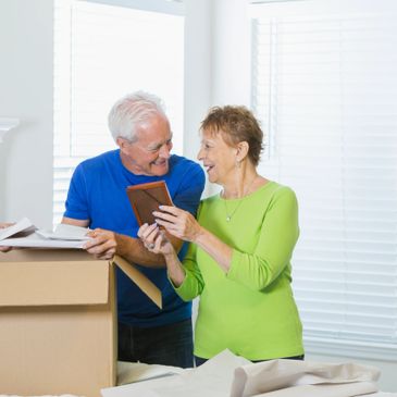 Elderly couple happily unpacking and sharing memories from a photo frame.