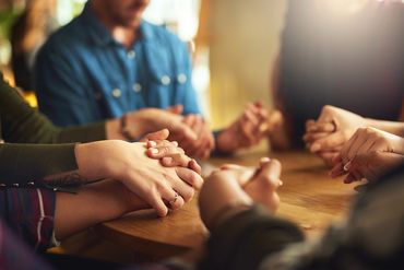 People holding hands in a circle around a table, showing support.