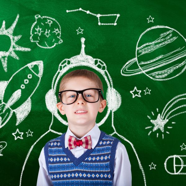 A boy with glasses stands in front of a chalkboard with space drawings.