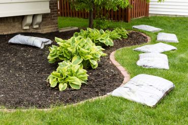 Garden bed with plants and mulch bags on the lawn.