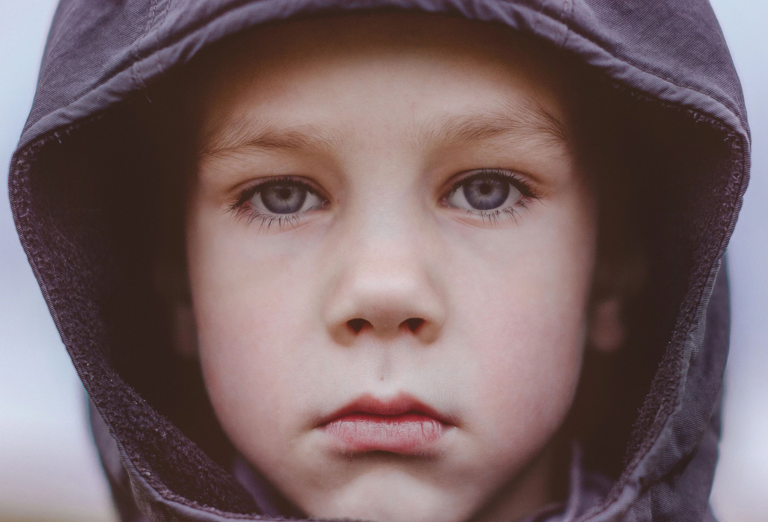 Close-up of a child with blue eyes wearing a dark hooded jacket.