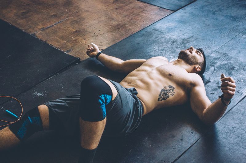 Young athlete resting in gym after hard cross training. Wearing professional sport clothing .