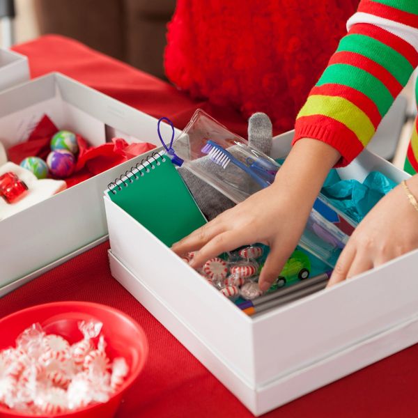 Hands packing a holiday gift box with essentials and candies.