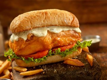 A crispy fish sandwich with lettuce, tomato, and creamy tartar sauce.