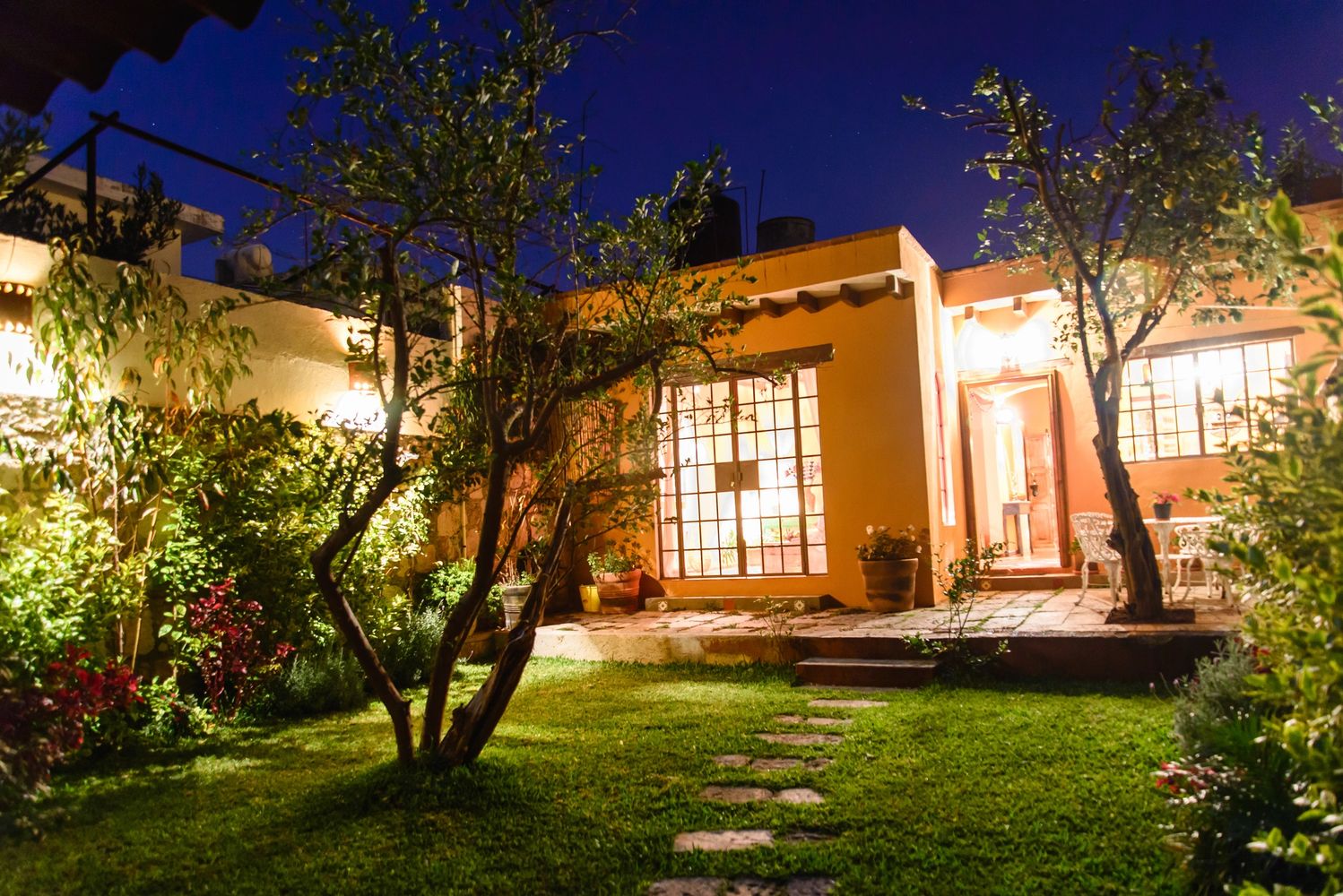 Cozy garden with illuminated house at night and stone path.
