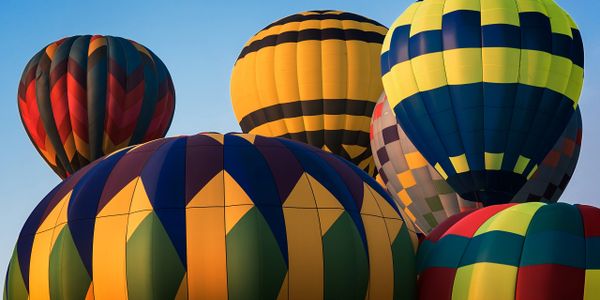 Colorful hot air balloons clustered against a clear blue sky.