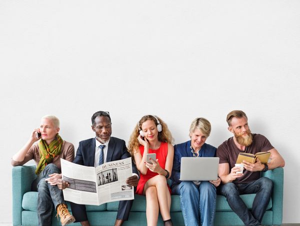 Five diverse people on a couch using various devices and reading.