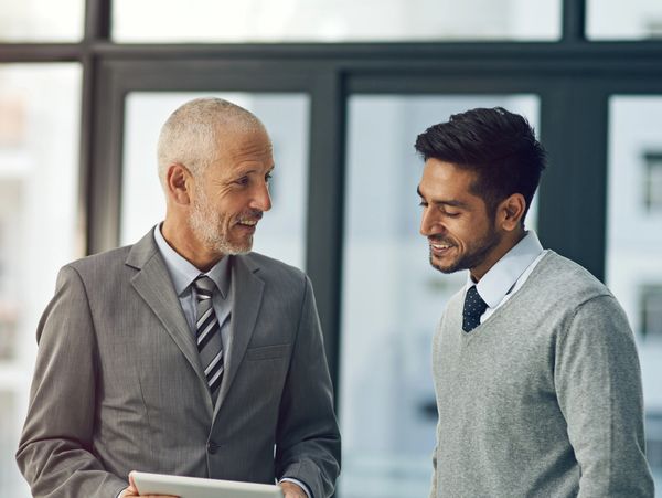 Two businessmen engaged in a friendly discussion using a tablet in an office.