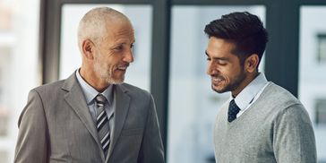 Two professional men engaged in a friendly conversation indoors.