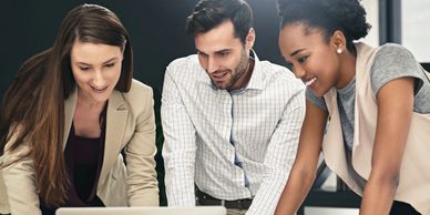 Three colleagues collaborate enthusiastically around a laptop in a modern office.
