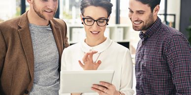 Three colleagues looking at a tablet and smiling in an office.