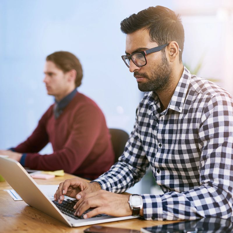 Shot of a businessman working on his laptop with his colleagues blurred in the background