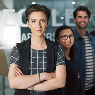 Confident businesswoman stands proudly with her diverse team in a modern office.