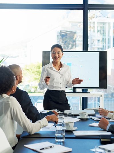A woman confidently presents to colleagues in a modern office meeting room.