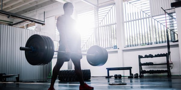 Person lifting heavy barbell in a gym with sunlight behind.