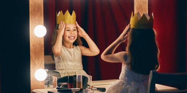 Girl wearing a golden crown and smiling at her mirror reflection.
