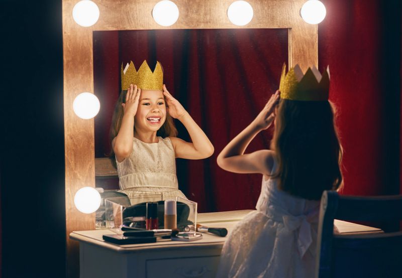 Cute little actress. Child girl in Princess costume on the background of theatrical scenes and mirrors.