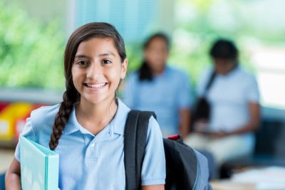 Smiling schoolgirl with books and backpack.