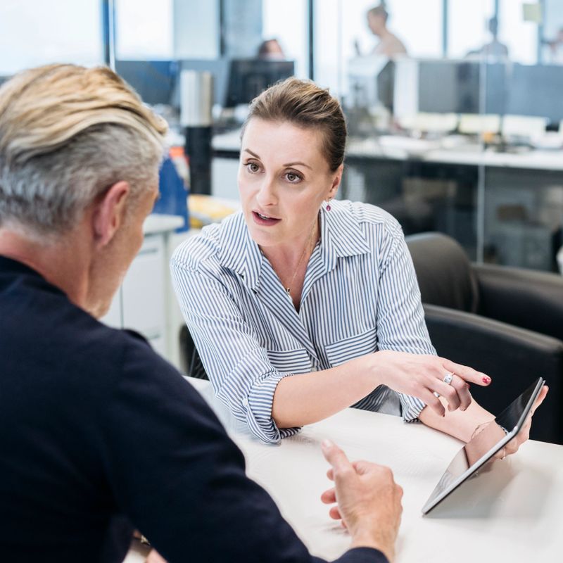 Mid adult woman and mature man in business meeting, two business people in office using tablet