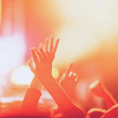 Hands raised in a crowd illuminated by warm, glowing light.