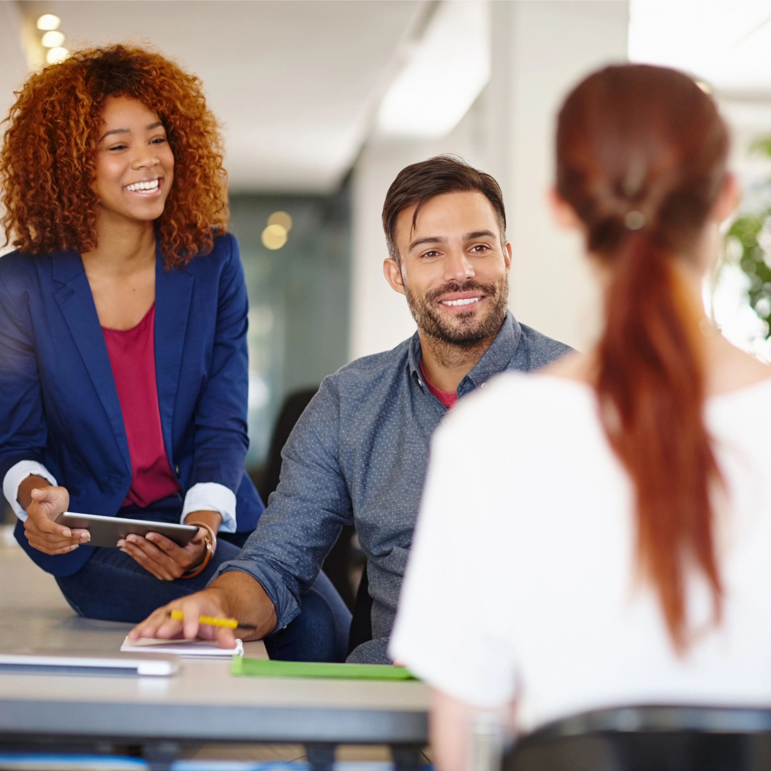 Two colleagues smiling and engaging in a conversation with a third person.