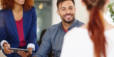 Two professionals smiling during a meeting with a colleague.