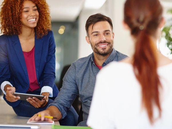 Three colleagues engaged in a friendly office discussion, smiling and attentive.