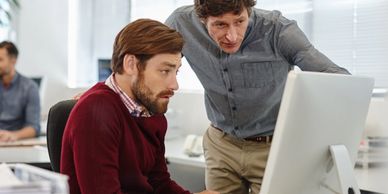 Two men collaborating and discussing work on a computer in an office.
