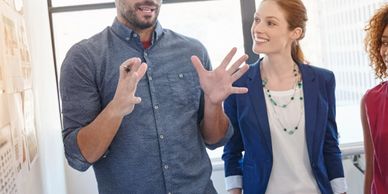 Man explaining ideas to two women in a bright office setting.