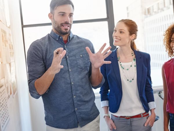 Man explaining ideas to two women in a bright office setting.