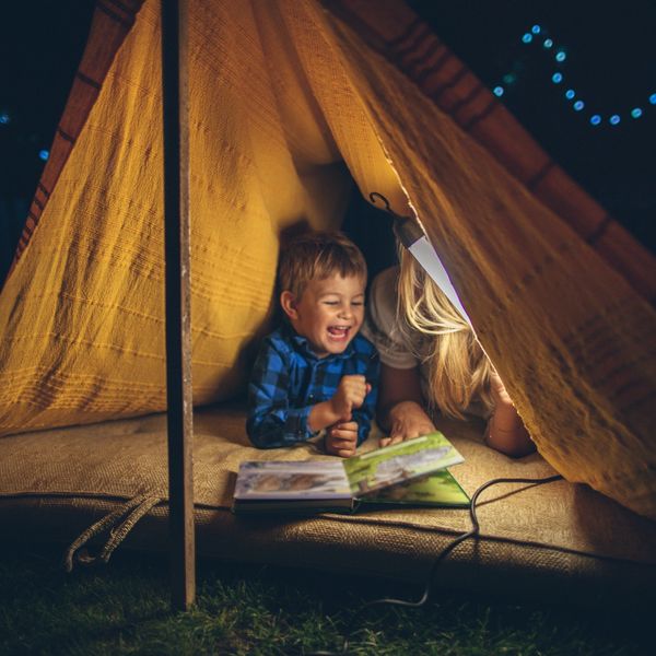 Child and adult reading inside a cozy tent at night.