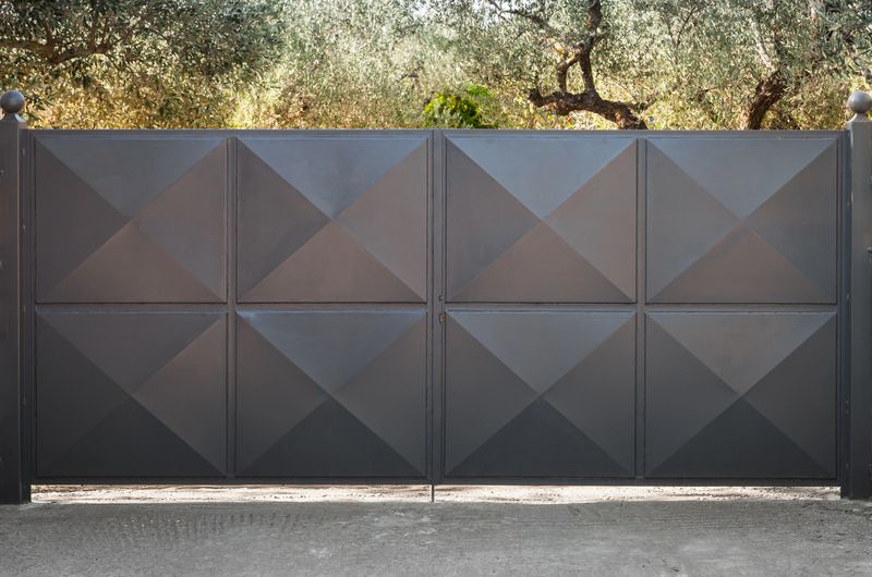 Black metal gate with square relief pattern and summer garden behind
