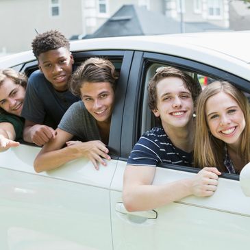 Five happy teenagers leaning out of a white car, smiling at the camera.
