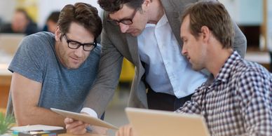 Three men collaborating on a tablet in a modern office.