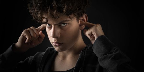 Teen boy with curly hair pressing his fingers to his temples, looking intense.