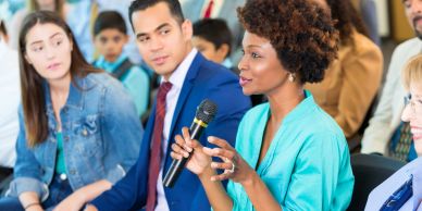 Woman speaking at a meeting with attentive listeners.