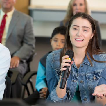 Young woman speaking into a microphone during a group discussion.
