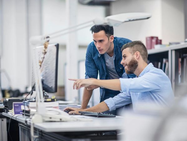 Two men collaborating and discussing work at a computer in a modern office.