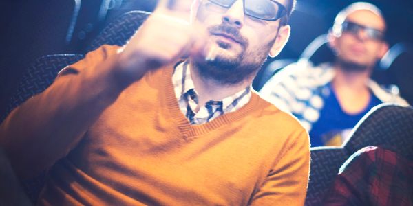 Man wearing 3D glasses giving a thumbs up in a movie theater.
