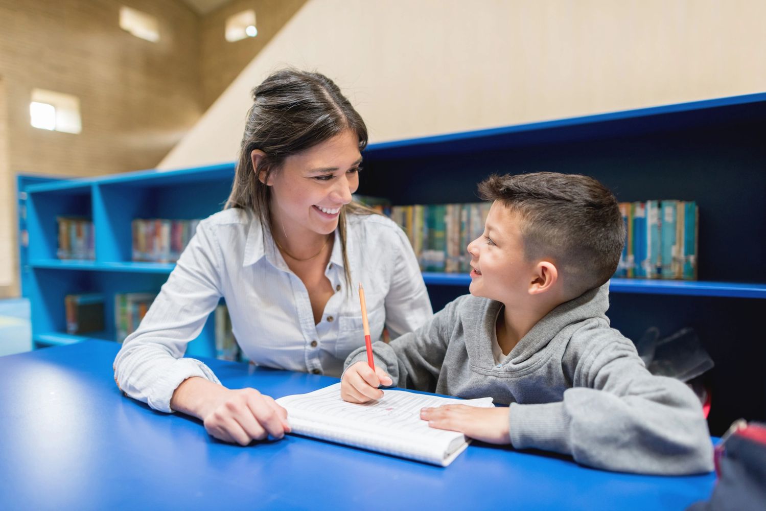 Teacher helping a young boy with his homework in a library.