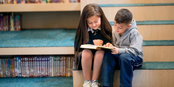 Two children reading a book together on library steps.