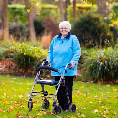 Elderly woman in blue jacket with walker outdoors in a park.