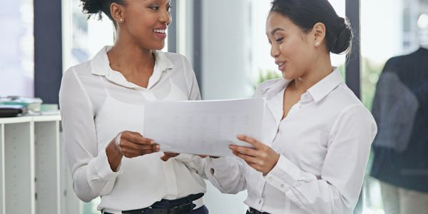 Two professional women discussing documents in a bright office.