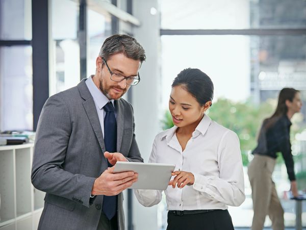 Two professionals discussing content on a tablet in an office.