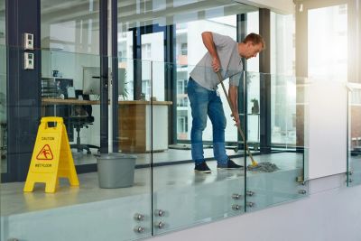 Man mopping floor inside a modern office with caution sign nearby.