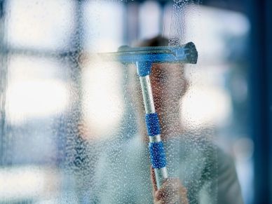 A person cleaning a glass window with a squeegee.