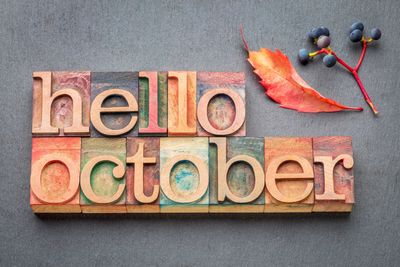 Wooden blocks spell out 'hello october' with fall leaves and berries.